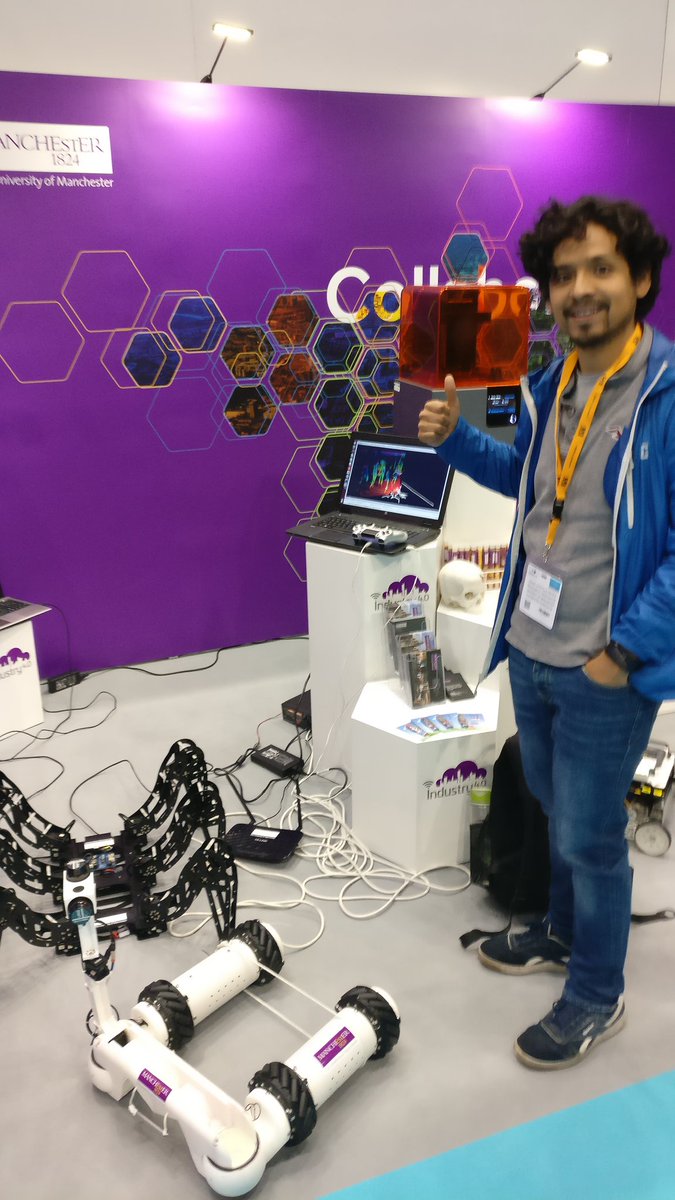 Dr. Omar Costilla Reyes beside a robotics and machine-learning demonstration at the University of Manchester stand.
