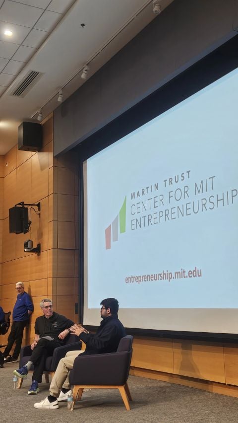Aravind Srinivas and Bill Aulet seated on stage in front of a Martin Trust Center for MIT Entrepreneurship screen.