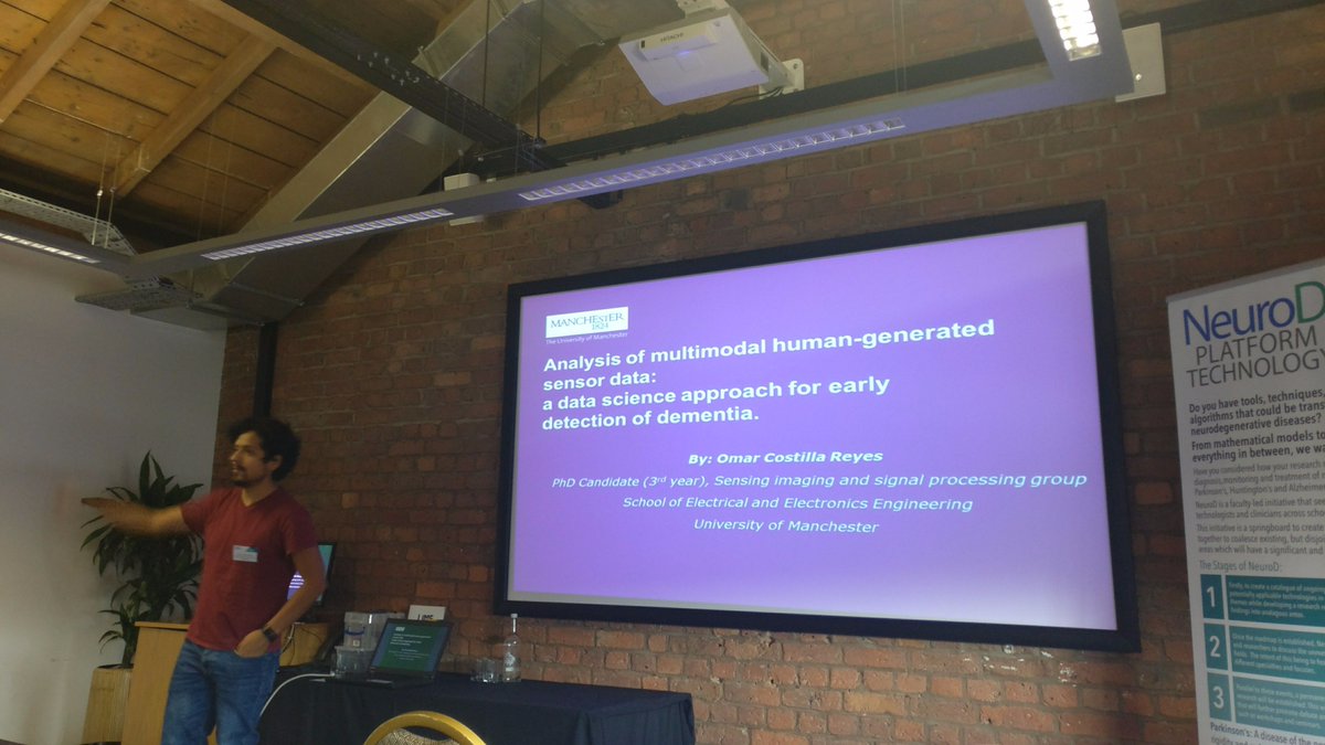 A presenter gestures toward a projected slide titled Analysis of multimodal human-generated sensor data: a data science approach for early detection of dementia.