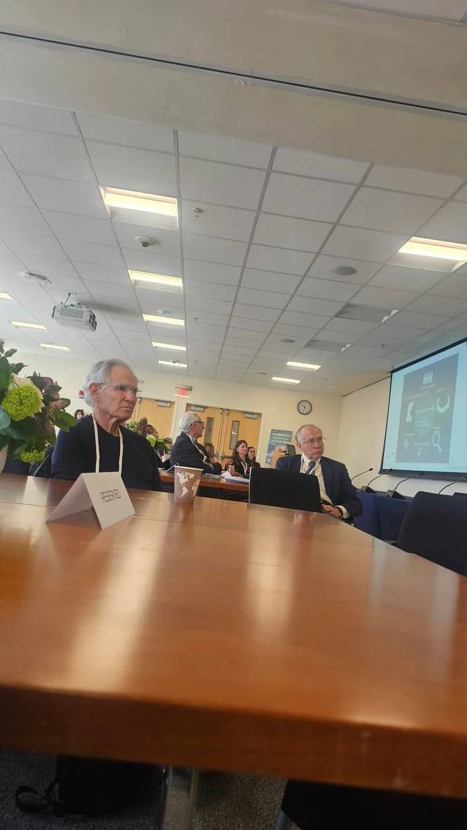Jon Kabat-Zinn seated at the conference table during the Harvard mindfulness symposium, seen from the neighboring seat.