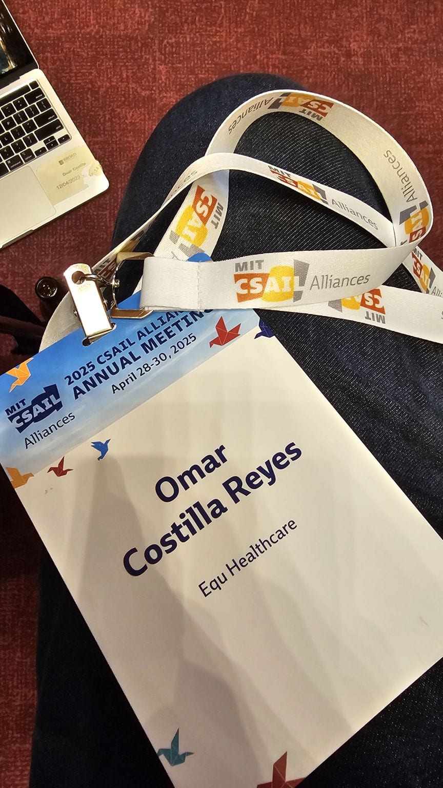 A 2025 CSAIL Alliances Annual Meeting badge reading Omar Costilla Reyes, Equ Healthcare, with an MIT CSAIL Alliances lanyard resting on a lap.