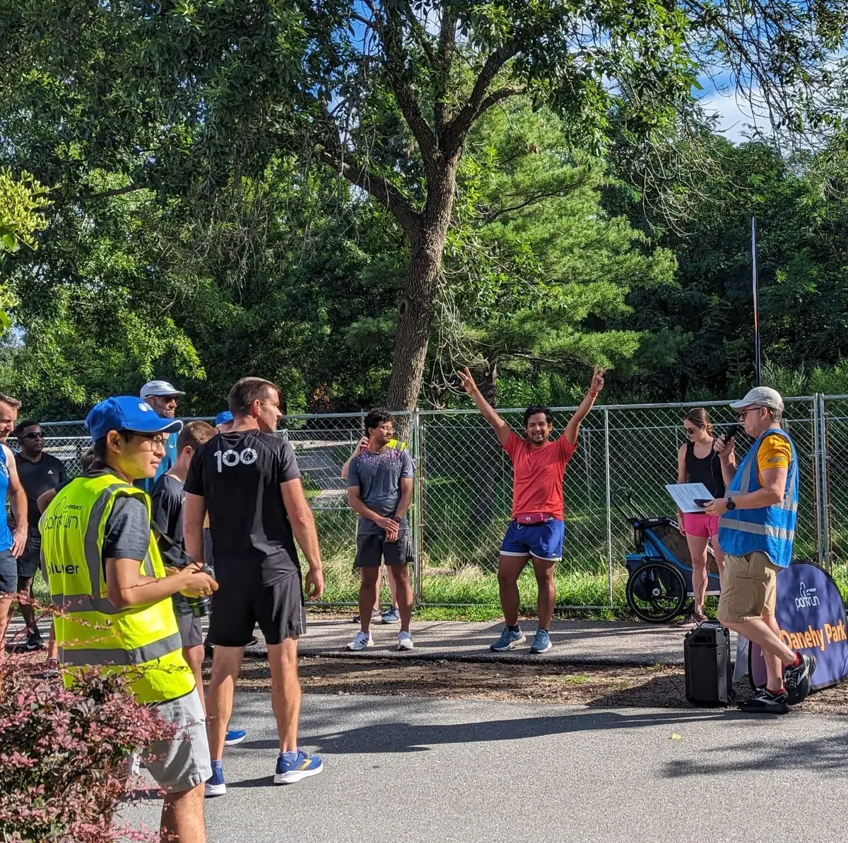 Omar raises his arms beside volunteers and runners at Danehy parkrun.