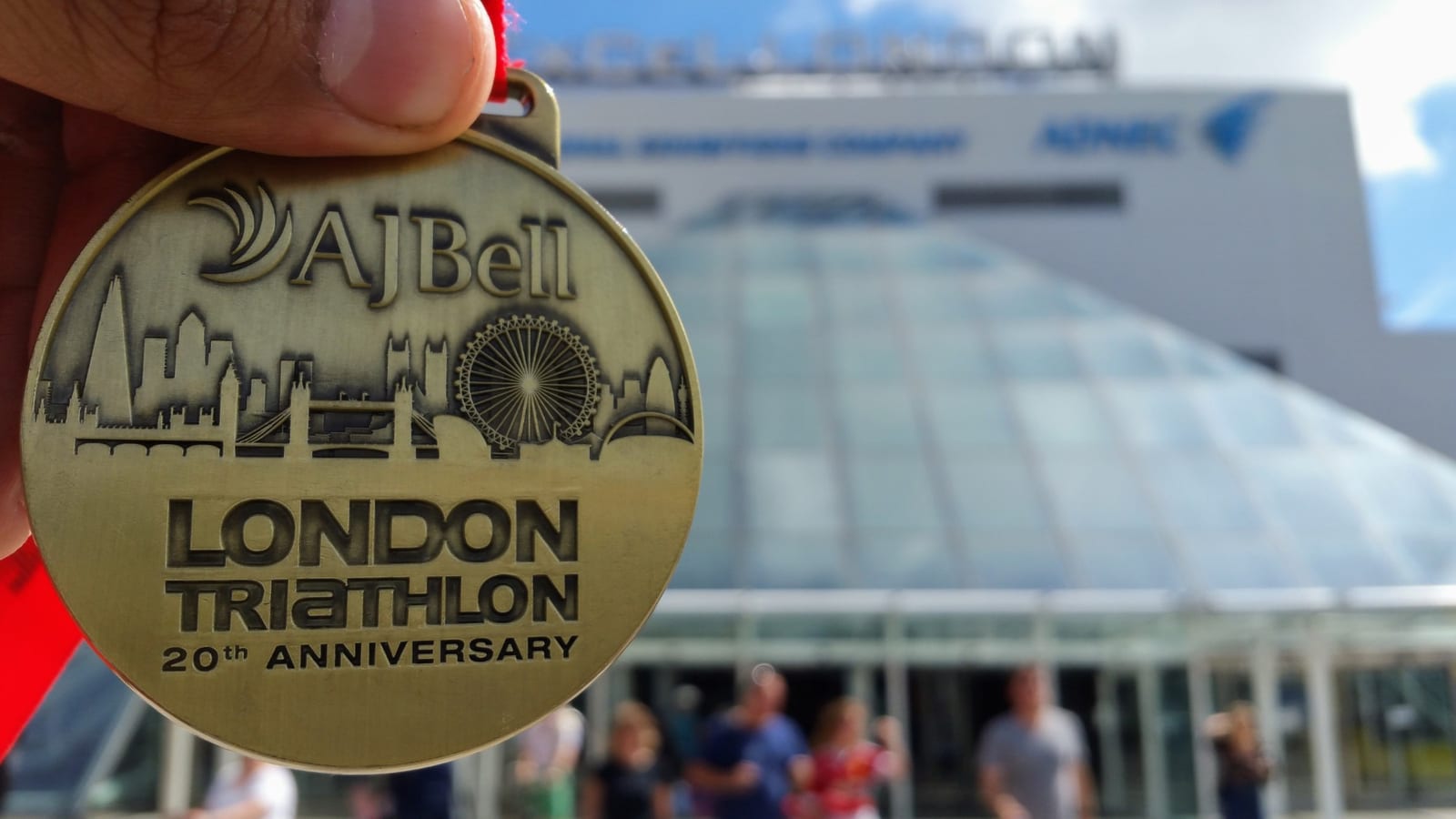 The AJ Bell London Triathlon 20th anniversary finisher’s medal held up in front of ExCeL London.