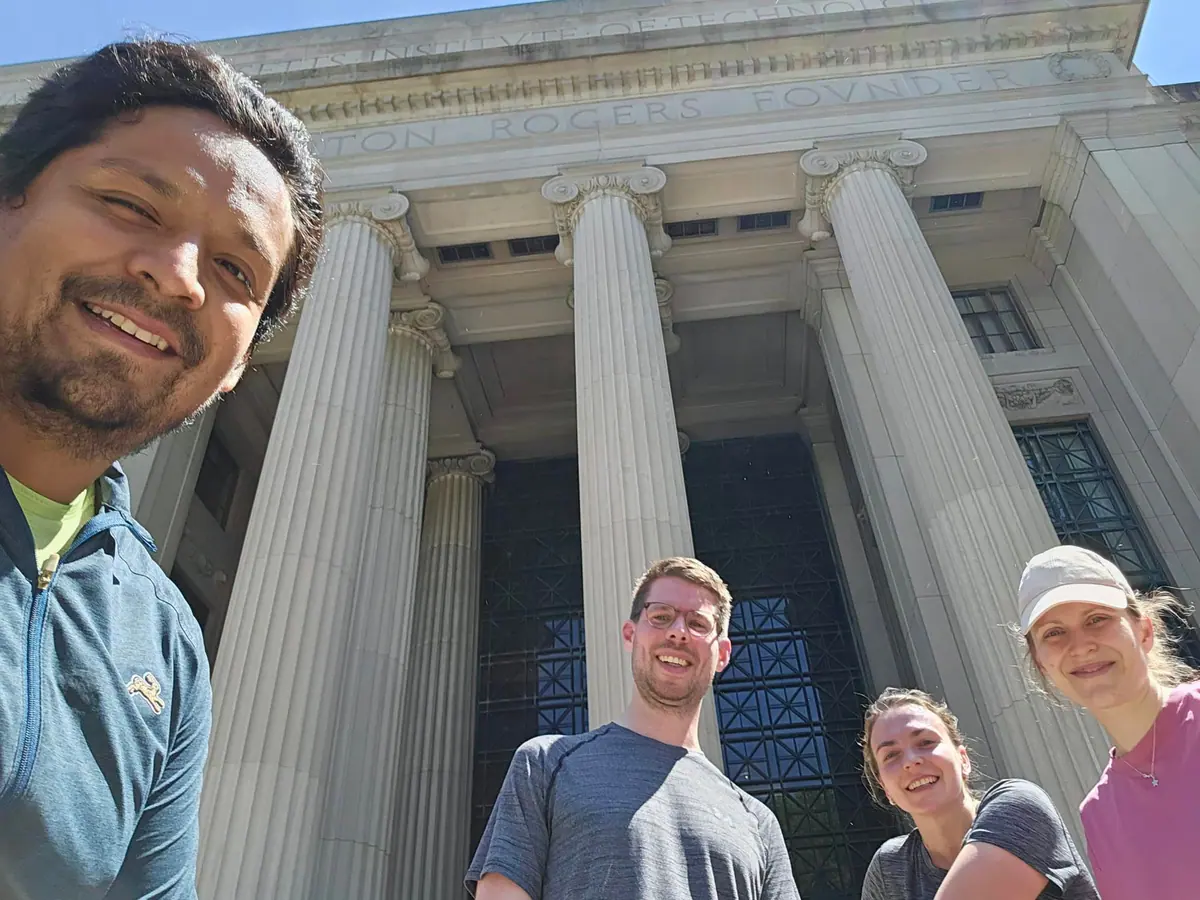 Omar and MIT postdoctoral friends take a group selfie outside the campus columns.