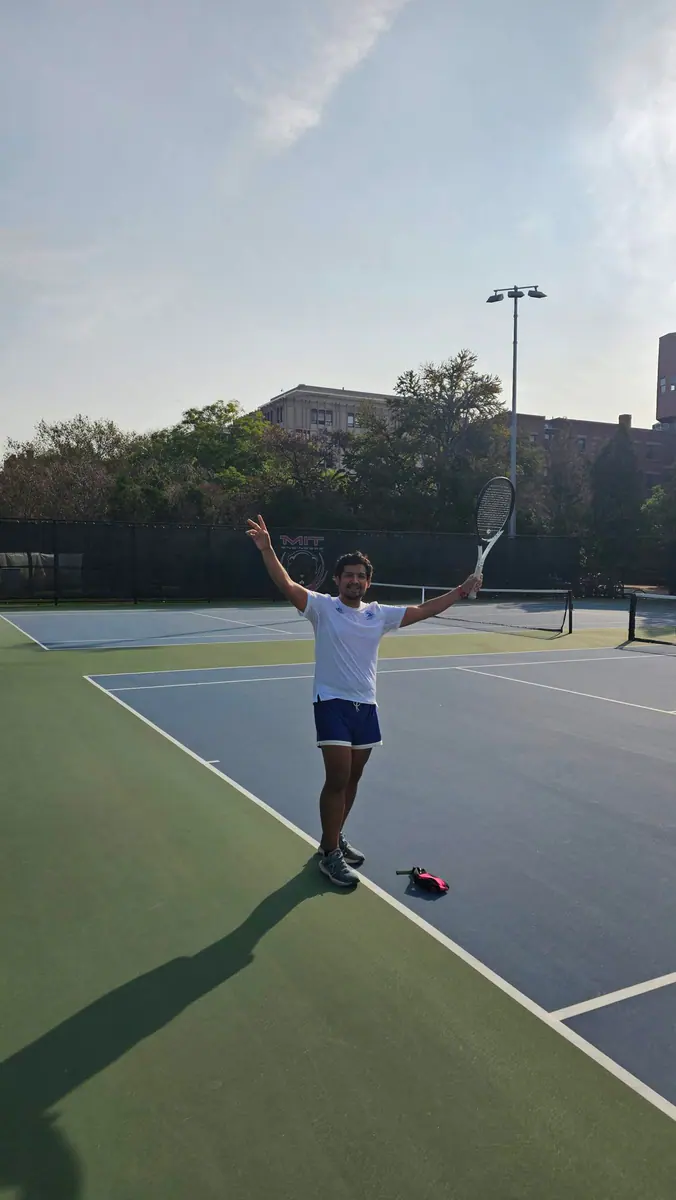 Omar holding a tennis racquet on an MIT tennis court.