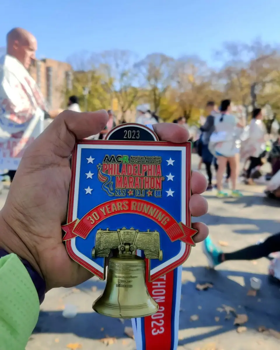 Philadelphia Marathon 2023 medal held up with the finish-area crowd behind it.