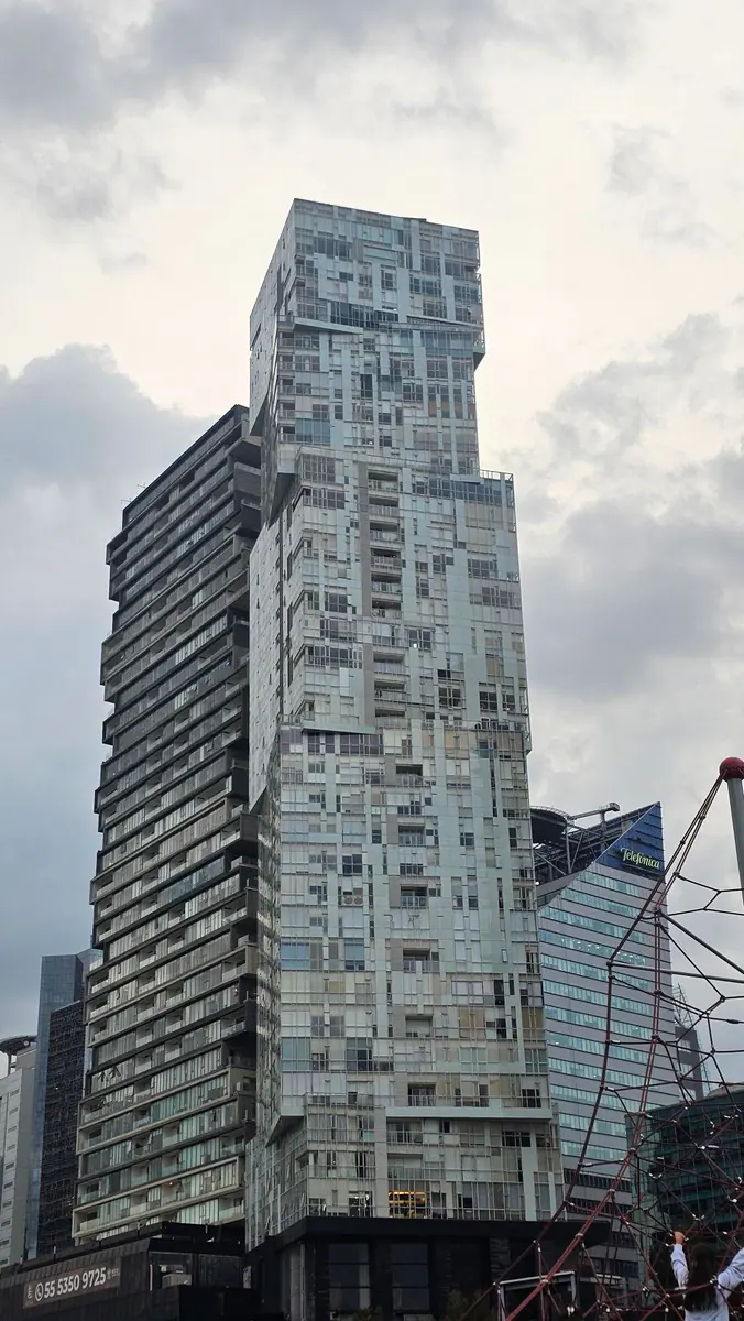 A tall, block-like glass tower rises above the Santa Fe skyline in Mexico City.